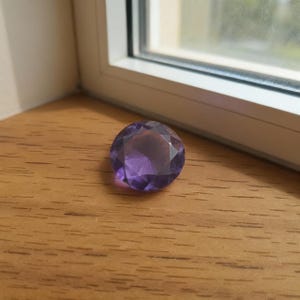 Round cut purple sapphire gemstone on wooden surface