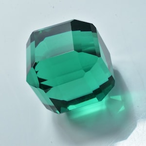 May include: A large, faceted, green glass paperweight. The paperweight is shaped like a cube with rounded edges.
