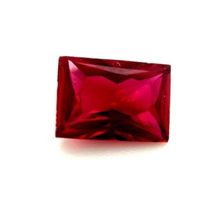 May include: A deep red rectangular gemstone with a faceted cut.