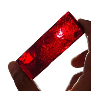 May include: A deep red, rectangular, translucent block of resin with air bubbles trapped inside. The resin is smooth and shiny.
