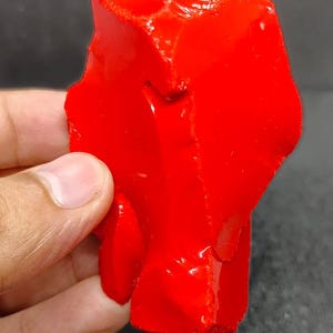 Puede incluir: Una pieza grande de obsidiana roja de forma irregular. La obsidiana tiene una superficie brillante, casi húmeda.