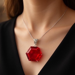 May include: A silver necklace with a large, red, hexagonal pendant. The pendant is faceted and hangs from a delicate silver chain. The necklace is shown against a dark background, highlighting the red gemstone.
