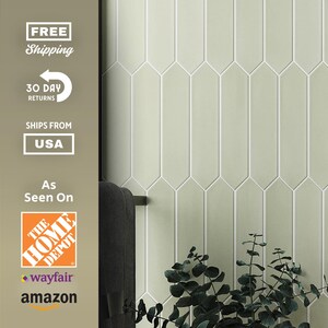 May include: Pale green elongated tile backsplash with white grout lines. The tiles are arranged vertically, creating a sleek, modern look. The image also includes a dark towel bar and a sprig of greenery.