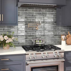 May include: A kitchen with gray subway tile backsplash, a stainless steel stove with a black burner grate, and a pot on the stovetop.