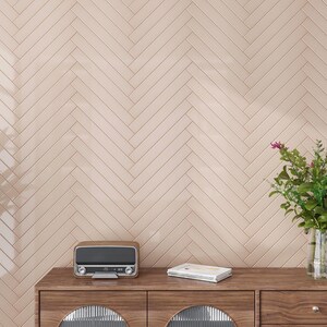 May include: A wooden dresser with two drawers and a light brown finish. The dresser has a vintage radio and a stack of books on top. The wall behind the dresser is covered in light pink herringbone tiles.