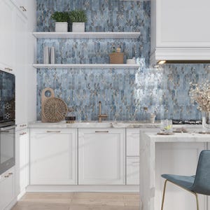 May include: White kitchen cabinets with gold hardware and a blue glass tile backsplash. The backsplash has a subtle floral pattern. There is a white countertop and a white island with a gold stool.