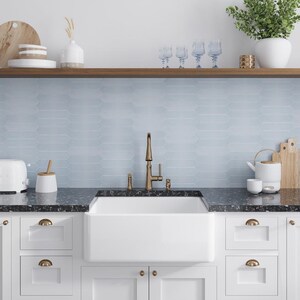May include: A white farmhouse style kitchen sink with a brushed gold faucet and a black granite countertop. The backsplash is light blue subway tile.