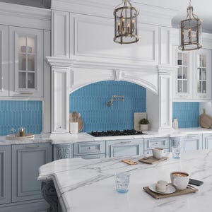 May include: A luxurious kitchen with white cabinetry, light blue accents, and a marble countertop. The backsplash features blue tile. Two pendant lights hang above the island, which has coffee cups and pastries. A gas stove is visible.