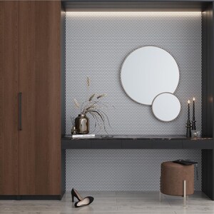 May include: A white hexagonal mosaic tile wall with a round mirror and a smaller round mirror. A brown vase with dried flowers sits on a black countertop with a brown stool.