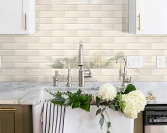 May include: A white farmhouse style kitchen sink with a brushed nickel faucet and a bouquet of white flowers. The sink is set against a backdrop of white subway tile.