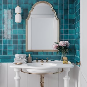 May include: A white porcelain bathroom sink with gold-toned faucets and a gold-toned towel rack. The sink is mounted on a white pedestal with gold-toned accents. The sink is in front of a wall tiled with teal blue square tiles. A gold-framed arched mirror hangs above the sink. A bouquet of pink flowers is in a clear glass vase on the counter.