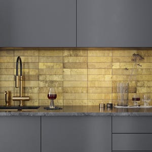 May include: A kitchen scene featuring a gold-toned backsplash, a black sink, and a gold faucet. A wine glass with red wine sits on the countertop. The cabinets are a dark gray color, and there are decorative candles and glasses.