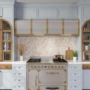 May include: A stainless steel range hood with brass accents is installed above a white and gold range with six burners. The range hood is mounted between white cabinets and a backsplash of beige and white mosaic tiles.