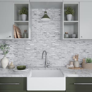 May include: A white kitchen sink with a chrome faucet and a white countertop. The backsplash is a white and gray mosaic tile. There are two open shelves above the sink, each with a potted plant and other decorative items.
