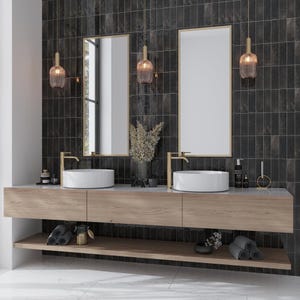 May include: A modern bathroom vanity with two sinks, gold faucets, and a floating shelf. The vanity is made of light wood and has a black tile backsplash. There are two gold pendant lights with clear glass shades hanging above the sinks.