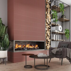 May include: A modern living room with a fireplace, a bookshelf, and a comfortable armchair. The fireplace is surrounded by red brick tiles and has a fire burning inside. The bookshelf is made of metal and has several shelves filled with books and plants. The armchair is upholstered in a dark gray fabric and has a throw blanket draped over it.