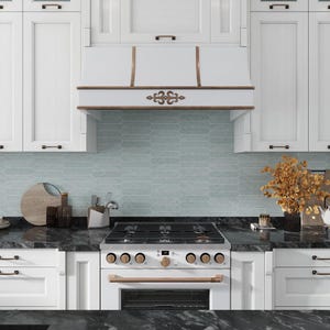 May include: A white kitchen with a stainless steel range and a white range hood with ornate brass accents. The backsplash is a light blue subway tile.