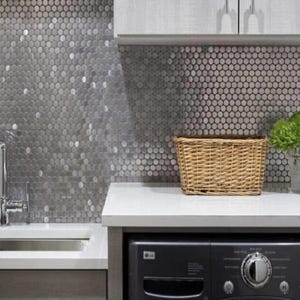 May include: A white countertop with a black washing machine and a wicker basket. The countertop and backsplash are covered in a silver penny tile.