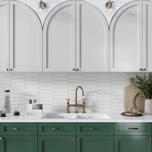 May include: A white kitchen with arched cabinets and green lower cabinets. The countertop is white with a double sink and a brass faucet. The backsplash is white subway tile.