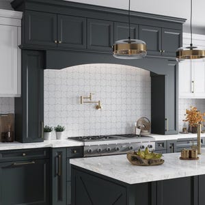 May include: A modern kitchen with dark gray cabinets, white subway tile backsplash with a geometric pattern, and a stainless steel gas stove. The kitchen features a large island with a white marble countertop and a gold faucet.