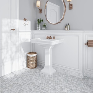 May include: A white pedestal sink with a white countertop and a white hexagonal tile floor. The sink has a brushed nickel faucet and a white ceramic basin. There is a wicker basket next to the sink.