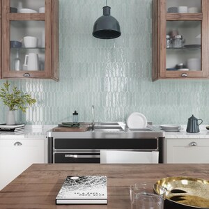 May include: A kitchen with light blue glass subway tiles, a stainless steel sink, and a black range. The countertop is made of white quartz. A book titled "In a dark, dark wood" is on the table.