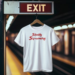 May include: White t-shirt with the text "Silently Screaming" in red script. The shirt hangs on a wooden hanger under an "EXIT" sign in a subway station. The background is blurred.