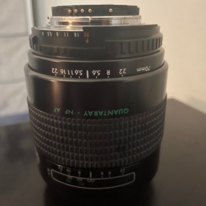 May include: A black 70mm camera lens with green text that reads "QUANTARAY - NF AF" and "70mm 22 R 5.6 5.6 11 16 22".