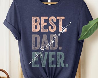 May include: Navy blue t-shirt with the text "Best Dad Ever" in a distressed font. The text is in shades of pink, gray, and green. The words "Ezra Noah" are written in cursive above the word "Dad" with a heart symbol.