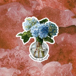 Könnte beinhalten: Ein Aufkleber mit einer Aquarellillustration von blauen Hortensien in einer klaren Glasvase. Die Vase steht auf einem rot-rosa Aquarellhintergrund. Der Text "susannah's hydrangeas" ist auf der Vase aufgedruckt.