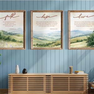Puede incluir: Tres impresiones enmarcadas con paisajes de acuarela y citas inspiradoras. Las impresiones presentan las palabras "fe", "esperanza" y "amor" con versículos bíblicos correspondientes.