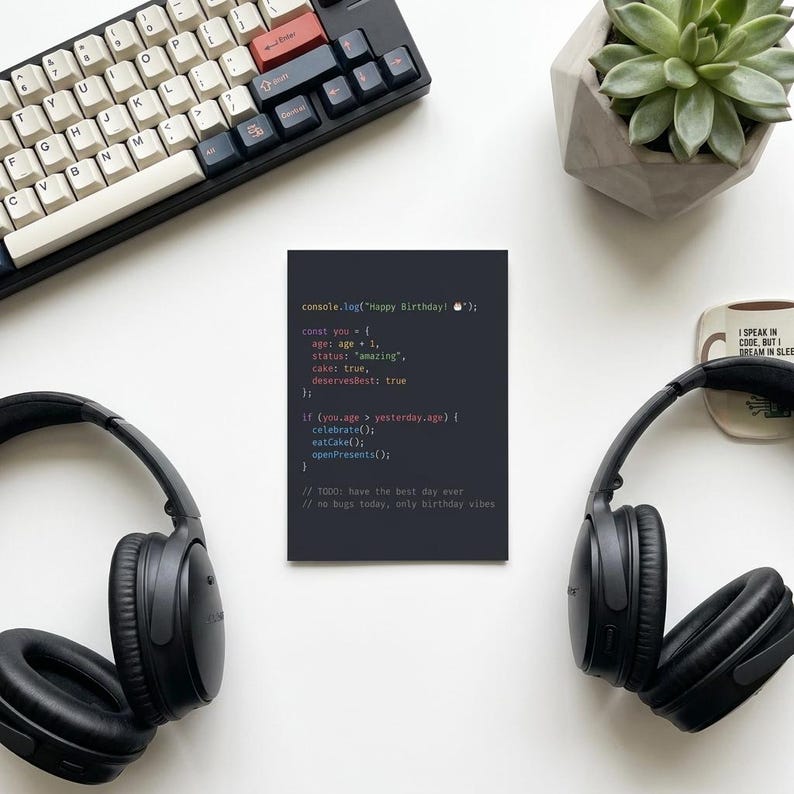 K&ouml;nnte beinhalten: Eine rechteckige Gru&szlig;karte mit dunkelgrauem Hintergrund und wei&szlig;em, rosa und orangefarbenem Computercode-Text, der lautet console.log("Happy Birthday! 🎂"); const you = { age: age + 1, status: "amazing", cake: true, deservesBest: true };