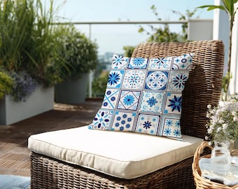 Könnte beinhalten: Ein quadratisches Zierkissen mit einem blau-weißen Fliesenmuster mit floralen und geometrischen Designs. Das Kissen liegt auf einem Korbstuhl mit cremefarbenem Kissen auf einer Terrasse.