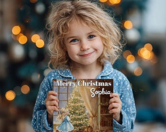 Puede incluir: Una niña en pijama azul sostiene un libro con temática navideña. La portada del libro presenta un árbol de Navidad, una niña con un vestido azul y el texto "Merry Christmas Sophia". El fondo incluye un árbol de Navidad borroso con luces bokeh.
