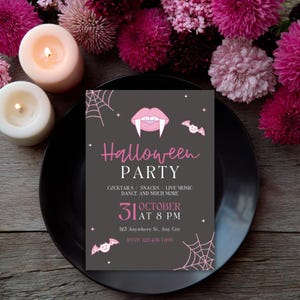 Op de afbeelding: Een Halloween-feestuitnodiging op een zwarte schaal, omringd door roze bloemen en kaarsen. De uitnodiging is donkergrijs met roze accenten, met een vampier mond, vleermuizen en spinnenwebben. Tekst bevat "Halloween Party" en evenement details.