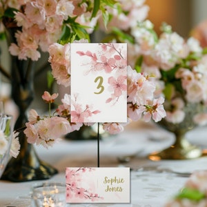 May include: Pink floral table number card with the number 3 printed in gold. A second card with the text "Sophie Jones" is also visible.