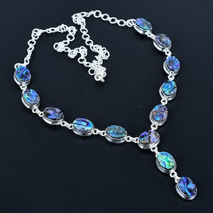 Puede incluir: Un collar de plata con una cadena larga y múltiples colgantes ovalados de concha de abulón. El collar tiene un brillo iridiscente azul, verde y morado.