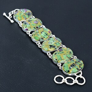 May include: A silver bracelet with seven oval-shaped green and gold stones. The stones have a mosaic-like pattern with flecks of red.