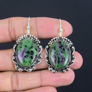 May include: A pair of silver earrings with green and pink oval-shaped gemstones set in ornate silver frames.