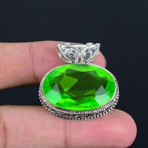 以下が含まれることがあります： 銀製のペンダント。楕円形の緑色の宝石が、細工の施された銀の枠にセットされています。ペンダントには装飾的なベイルが付いています。