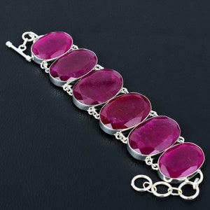 Puede incluir: Una pulsera de plata con seis piedras ovaladas de color rosa oscuro. La pulsera tiene un cierre de palanca.