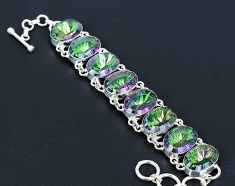 Peut inclure: Un bracelet en argent orné de pierres précieuses ovales et irisées, aux tons verts et violets. Les pierres sont serties dans des chatons individuels en argent et reliées par une chaîne délicate. Le bracelet est doté d'un fermoir à bascule.