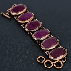 May include: A copper bracelet with a chain link design and seven oval-shaped purple gemstones.