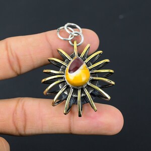 May include: A pendant featuring a teardrop-shaped, multi-colored stone set in a silver and gold-toned metal flower design. The stone has a mix of yellow, brown, and white hues. The pendant is held by a silver bail.