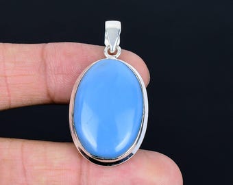 May include: Oval-shaped, light blue pendant with a silver-colored metal frame. The pendant has a smooth, polished surface and a small loop at the top for a chain. The background is black.