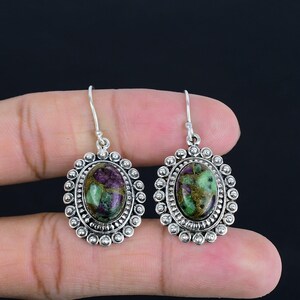 Könnte beinhalten: Ein Paar silberne Ohrringe mit ovalen grünen und violetten Edelstein-Cabochons, die in einer silbernen Fassung mit einer perlenbesetzten Kante gefasst sind.
