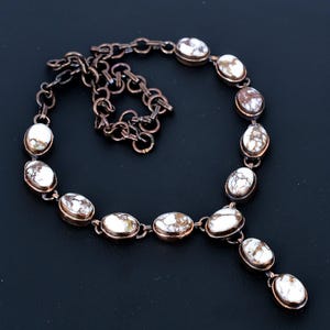 May include: A copper-toned necklace featuring oval-shaped white and brown stones. The stones are set in a copper-colored metal and connected by a chain. The necklace has a Y-shaped pendant design with three dangling stones.