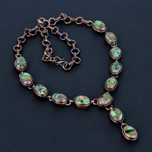 Puede incluir: Un collar de cadena de cobre con un colgante y piedras ovaladas de color verde y rosa.