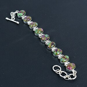 Puede incluir: Una pulsera de plata con nueve piedras cabujón ovaladas que presentan un patrón moteado en magenta intenso, verde bosque y negro. Las piedras están engastadas en biseles de plata pulida y unidas por eslabones de plata con cierre de barra.
