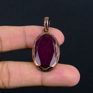 May include: A copper pendant with a large oval-shaped purple gemstone. The pendant has a detailed, textured copper frame.